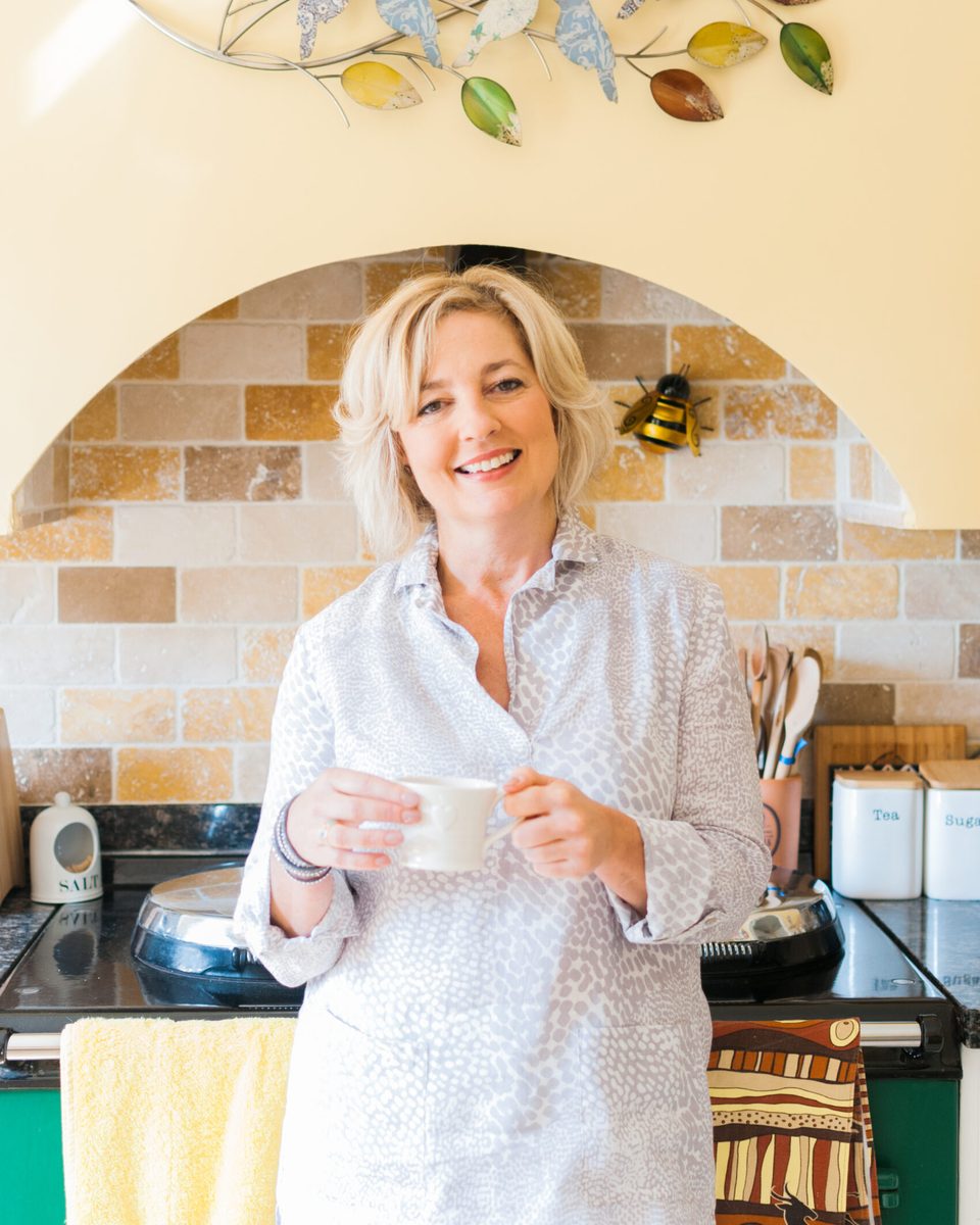 Lynne James smiling with a cup of tea in her kitchen