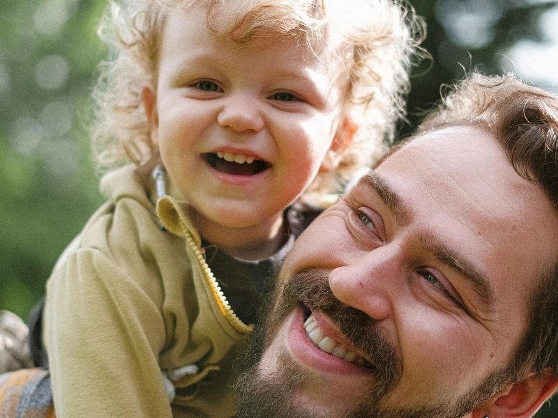 A father laughing with his young child on his shoulders